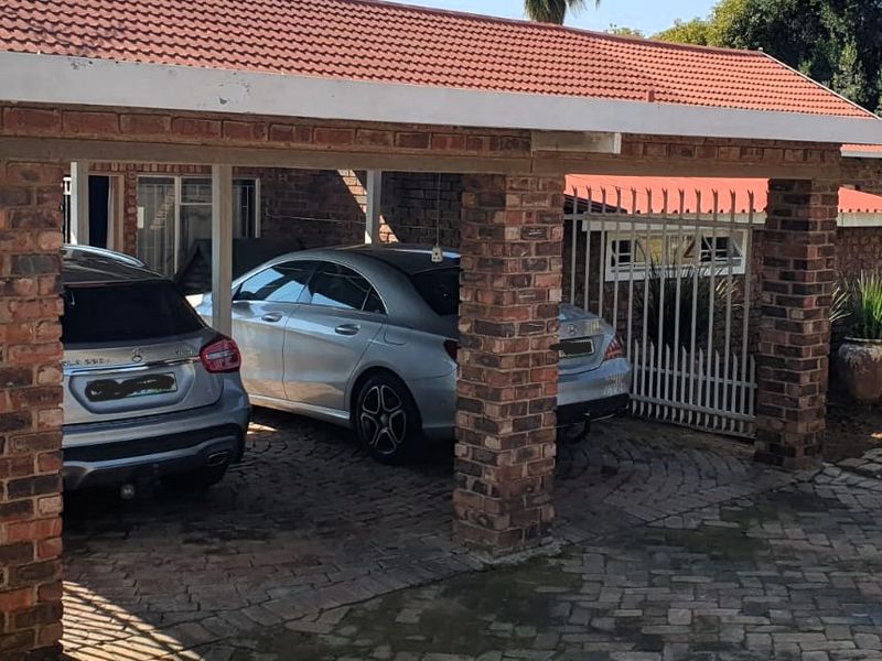 A covered carport area featuring exposed brick pillars, a tiled roof, and paved flooring, providing sheltered parking space.