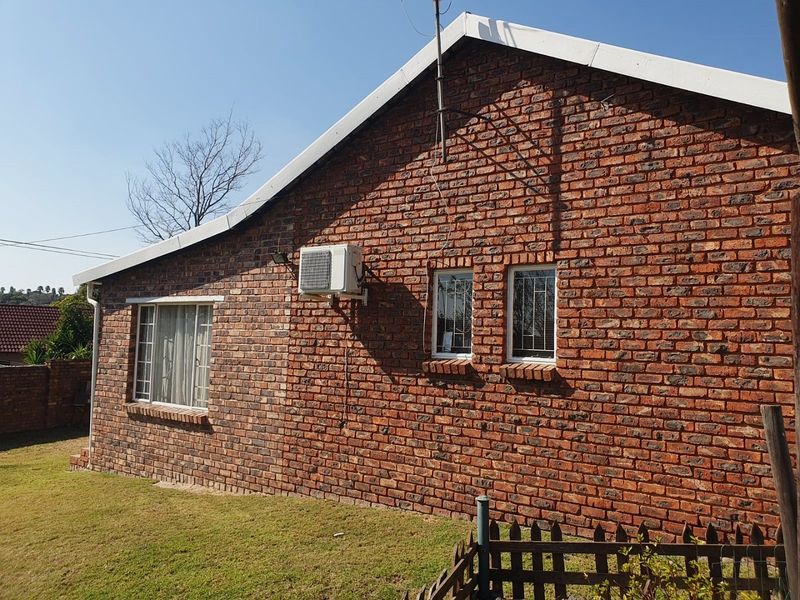 A side view of the house featuring a face brick exterior, white fascia boards, security bars on windows, and an external air conditioning unit.