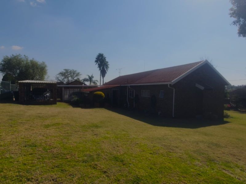 A view of the rear exterior of the house featuring a brick facade, tiled roof, and an attached carport set within a large lawn area.