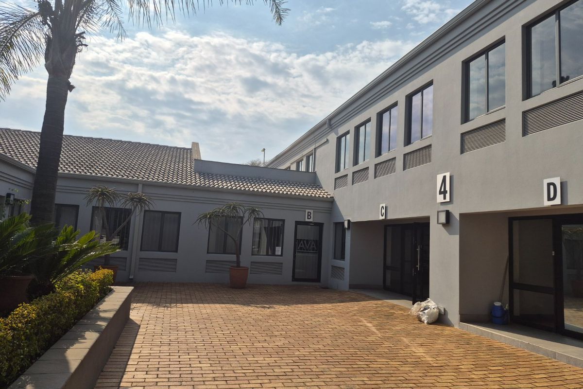 A well-maintained commercial courtyard area featuring paved flooring, modern grey facade, and multiple office unit entrances.
