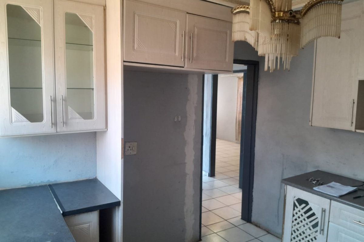 A dated kitchen space featuring fitted cabinetry and tiled flooring, currently requiring cosmetic updates and wall finishing to reach its full potential.