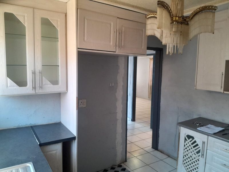 A dated kitchen space featuring fitted cabinetry and tiled flooring, currently requiring cosmetic updates and wall finishing to reach its full potential.