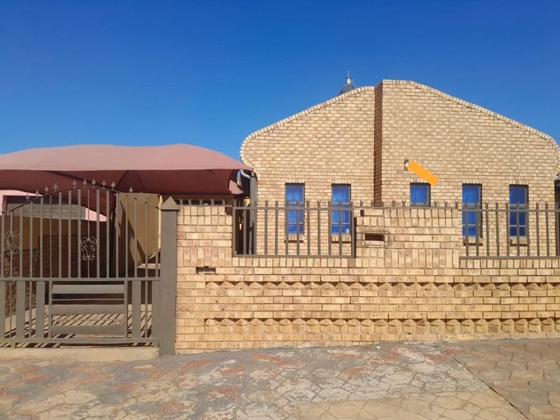 Front exterior view of a face brick house featuring a metal security gate, perimeter fencing, and a shade cloth carport over the driveway.