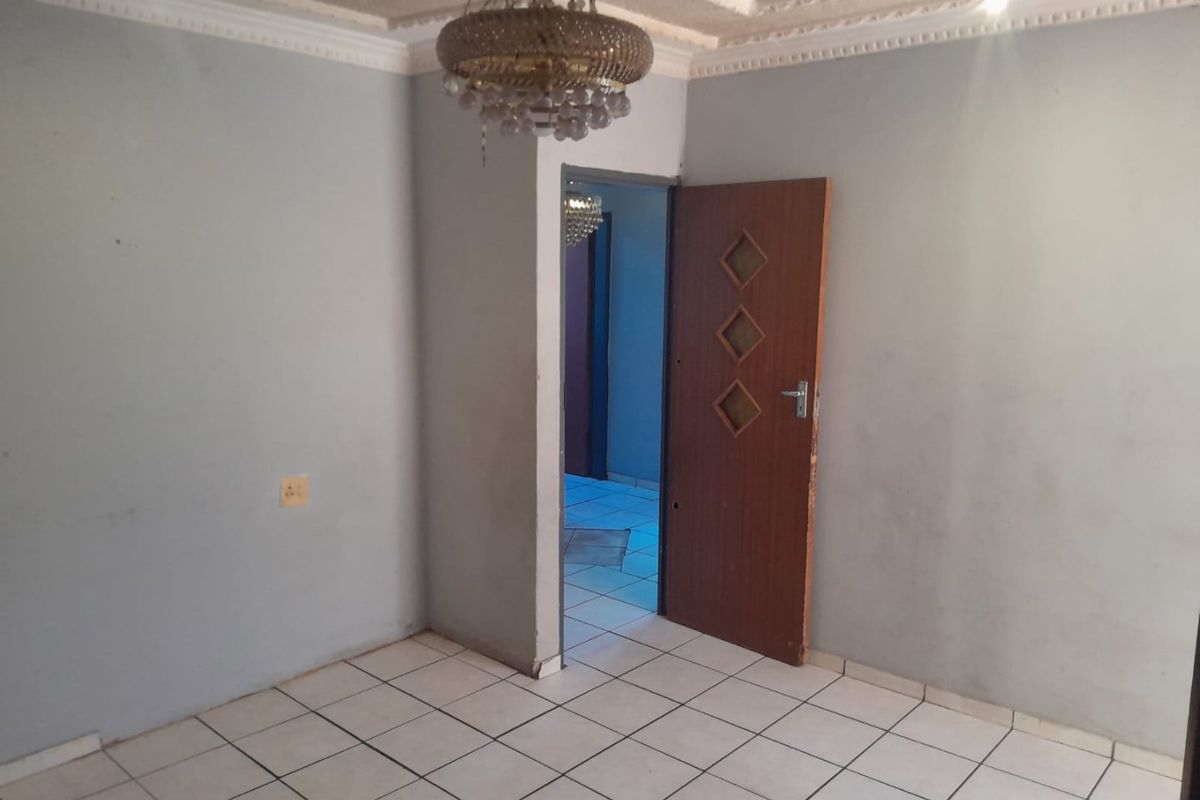 An empty living room featuring ceramic floor tiles, decorative ceiling cornicing, and a wooden internal door leading to an adjacent space.