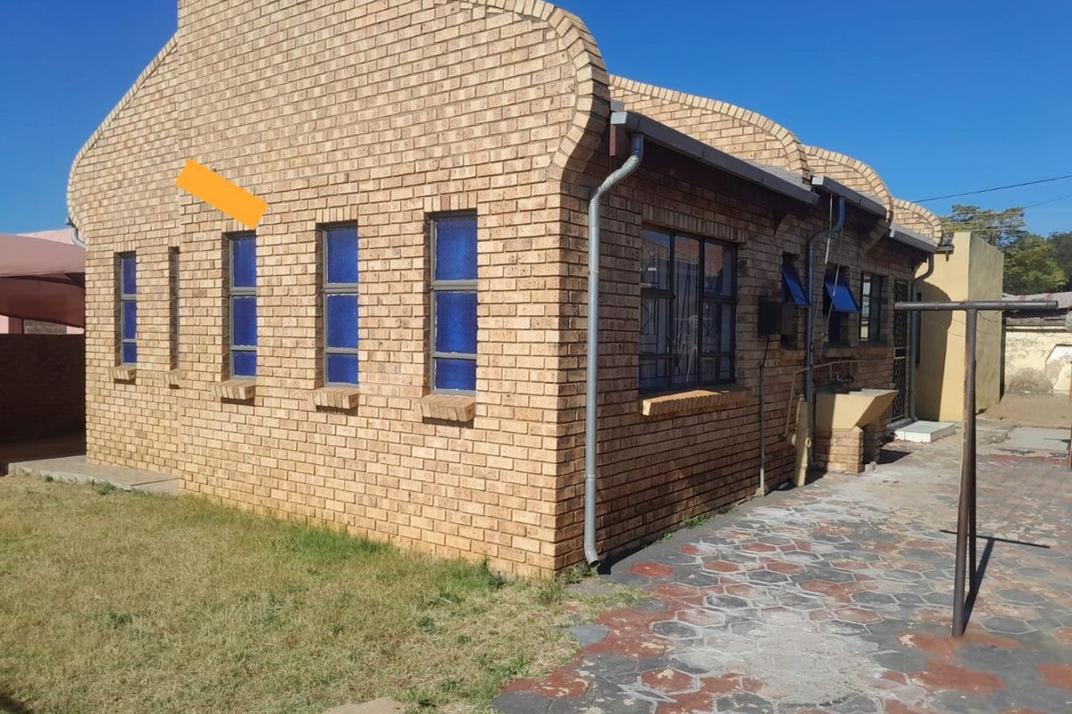 Rear view of a face brick house featuring steel-framed windows, a paved walkway, and an external utility sink area.
