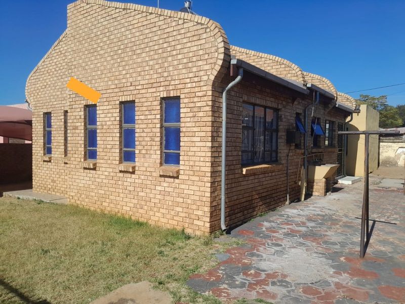 Rear view of a face brick house featuring steel-framed windows, a paved walkway, and an external utility sink area.