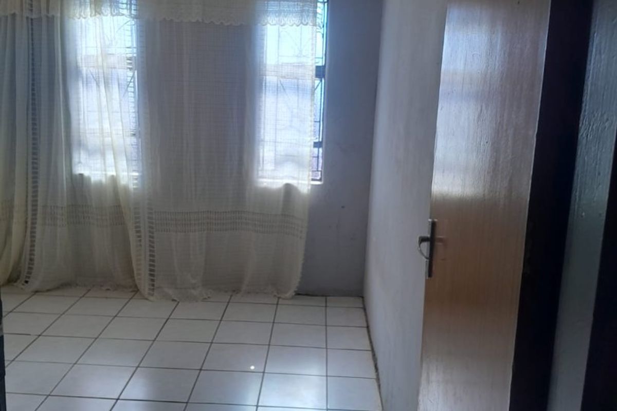 An empty bedroom featuring tiled flooring, decorative ceiling cornicing, and security bars on the windows, offering a blank canvas for renovation.