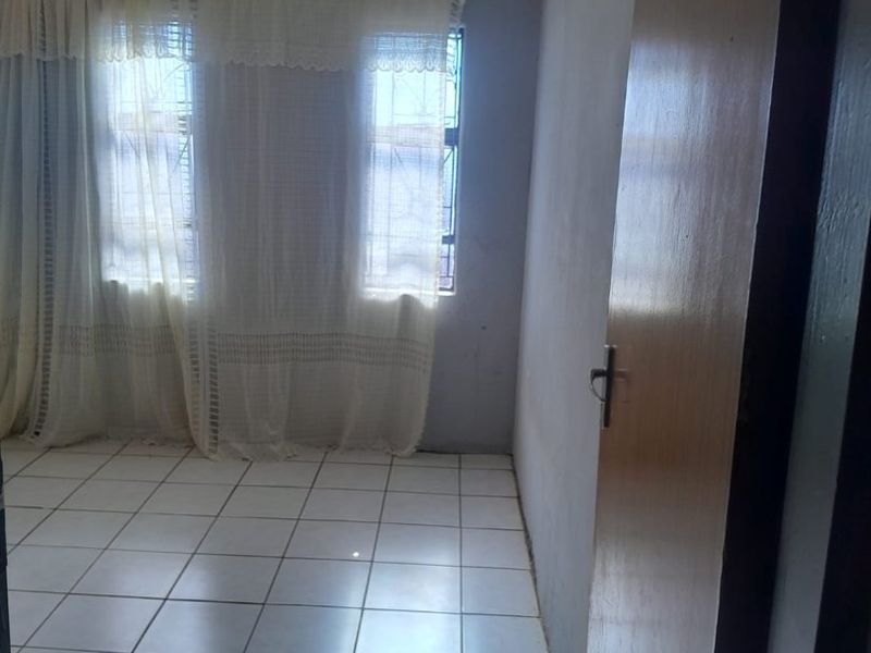 An empty bedroom featuring tiled flooring, decorative ceiling cornicing, and security bars on the windows, offering a blank canvas for renovation.