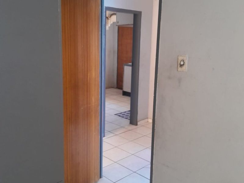 A view through a hallway featuring tiled flooring, a built-in cupboard, and access to adjacent rooms with visible wear on wall surfaces.