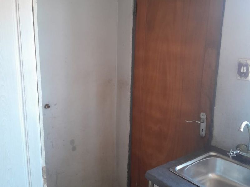 A functional scullery or utility area featuring a stainless steel sink, base cabinetry, and tiled flooring, requiring cosmetic updates to the walls and finishes.