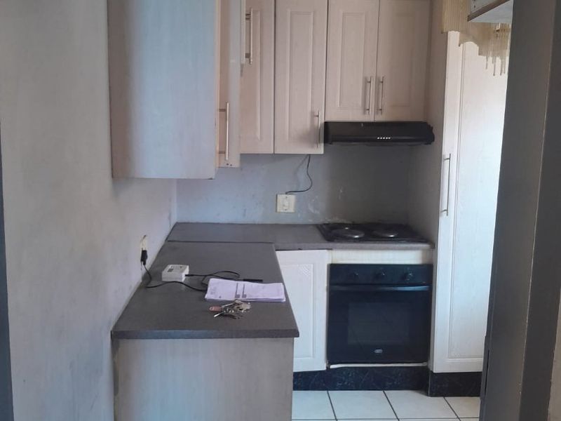 A compact kitchen featuring built-in cabinetry, an electric oven, hob, and extractor fan, with tiled flooring and potential for cosmetic updates.