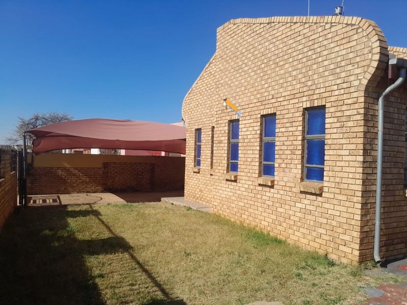 Rear view of the property featuring a face brick facade, a small lawn area, and a covered outdoor space with a shade sail.