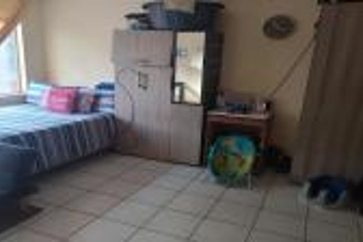 A bedroom featuring tiled flooring and a window, currently furnished with various personal items and storage units.