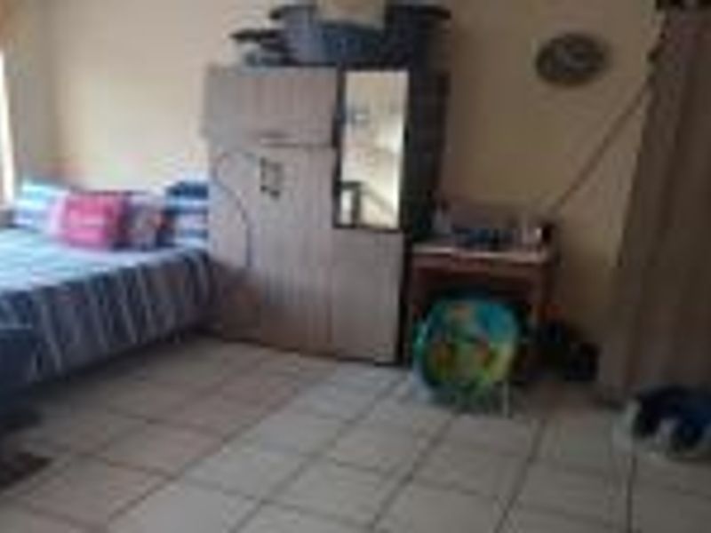 A bedroom featuring tiled flooring and a window, currently furnished with various personal items and storage units.