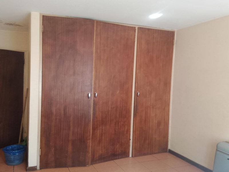 A bedroom featuring built-in wooden wardrobes, tiled flooring, and recessed lighting, showing signs of ceiling water damage and dated finishes.