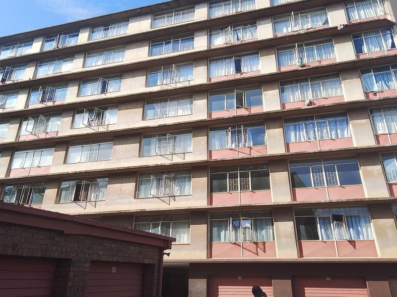 A multi-story apartment building facade featuring numerous casement windows and ground-level garage access.