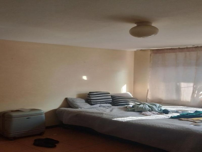 A simple bedroom featuring tiled flooring, a window with security bars, and a central ceiling light fixture.