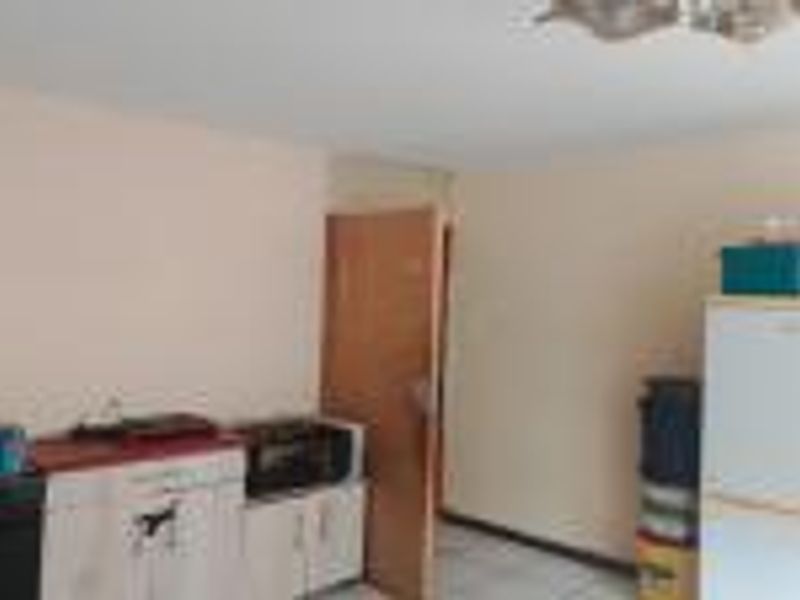 A functional kitchen area featuring basic cabinetry, countertop space, and tiled flooring, currently showing signs of wear and dated finishes.