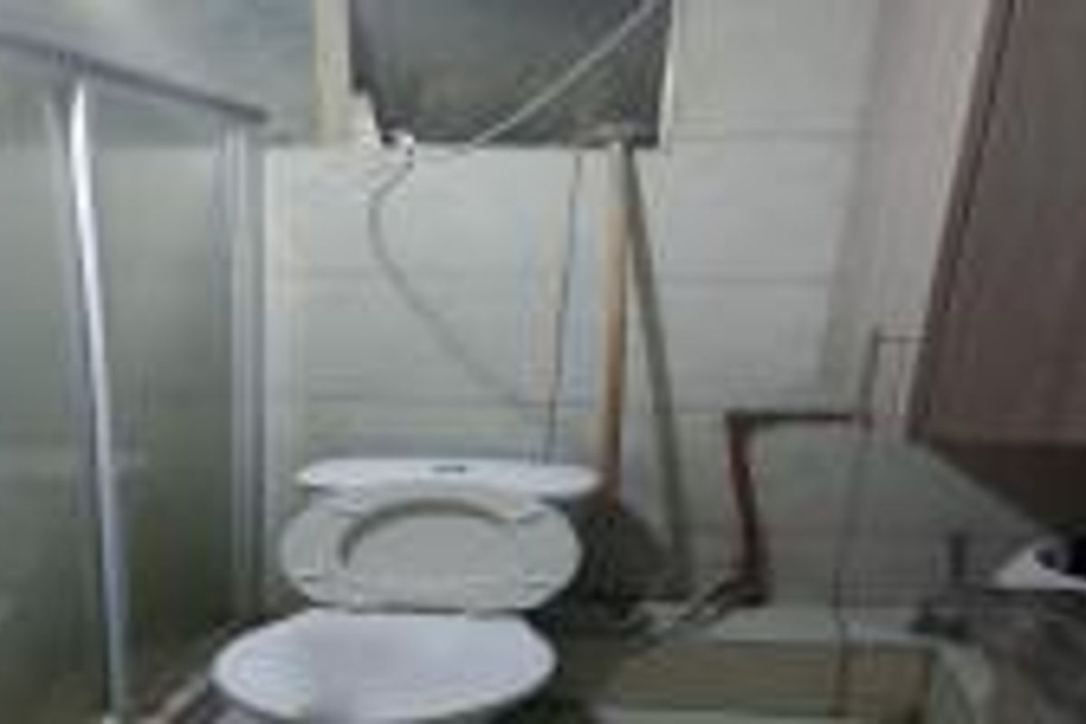 A bathroom featuring a toilet and shower enclosure, currently showing signs of unfinished wall work and exposed plumbing.