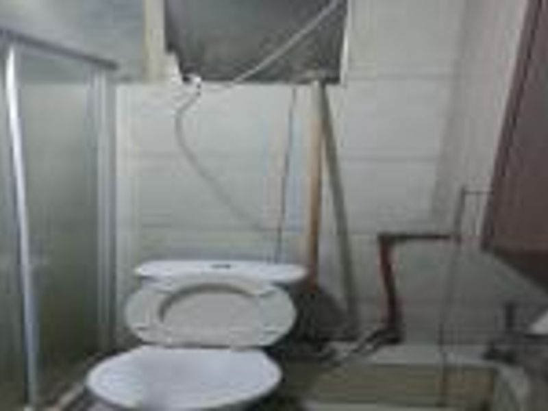 A bathroom featuring a toilet and shower enclosure, currently showing signs of unfinished wall work and exposed plumbing.