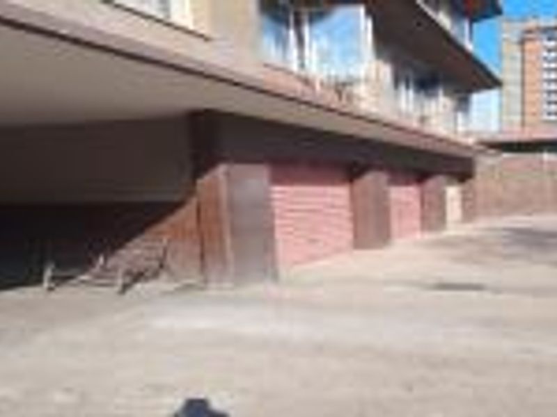 A covered parking area featuring multiple roller shutter garage doors and a concrete driveway in an apartment complex setting.