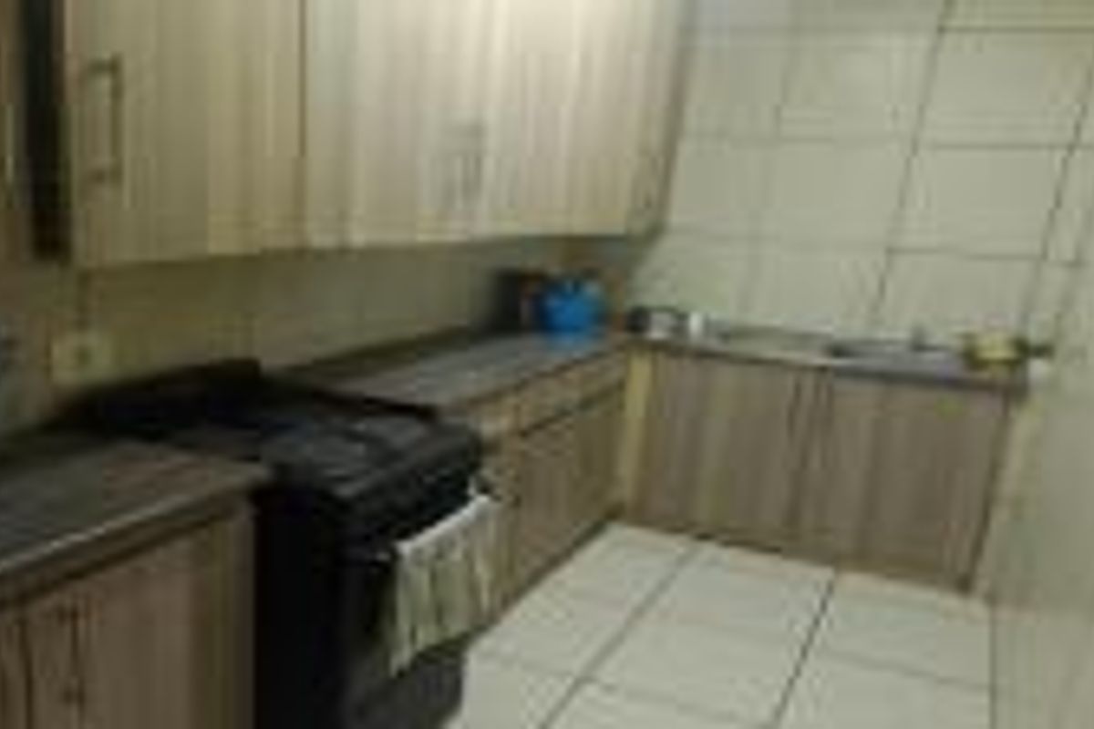 A compact kitchen featuring laminate cabinetry, tiled walls, and flooring. The space is functional but dated, offering potential for a modern renovation.