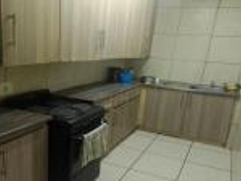 A compact kitchen featuring laminate cabinetry, tiled walls, and flooring. The space is functional but dated, offering potential for a modern renovation.