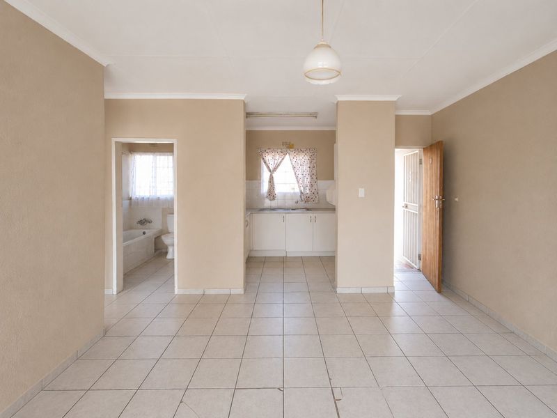 Open plan living area featuring tiled floors, leading to a functional kitchen and a separate bathroom with a bathtub and toilet.