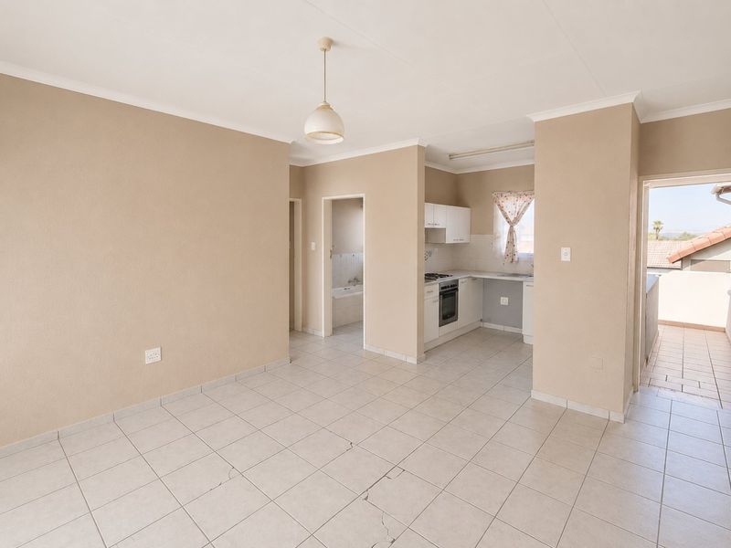 Open-plan living area featuring tiled flooring, a compact kitchen with built-in appliances, and direct access to an outdoor balcony.
