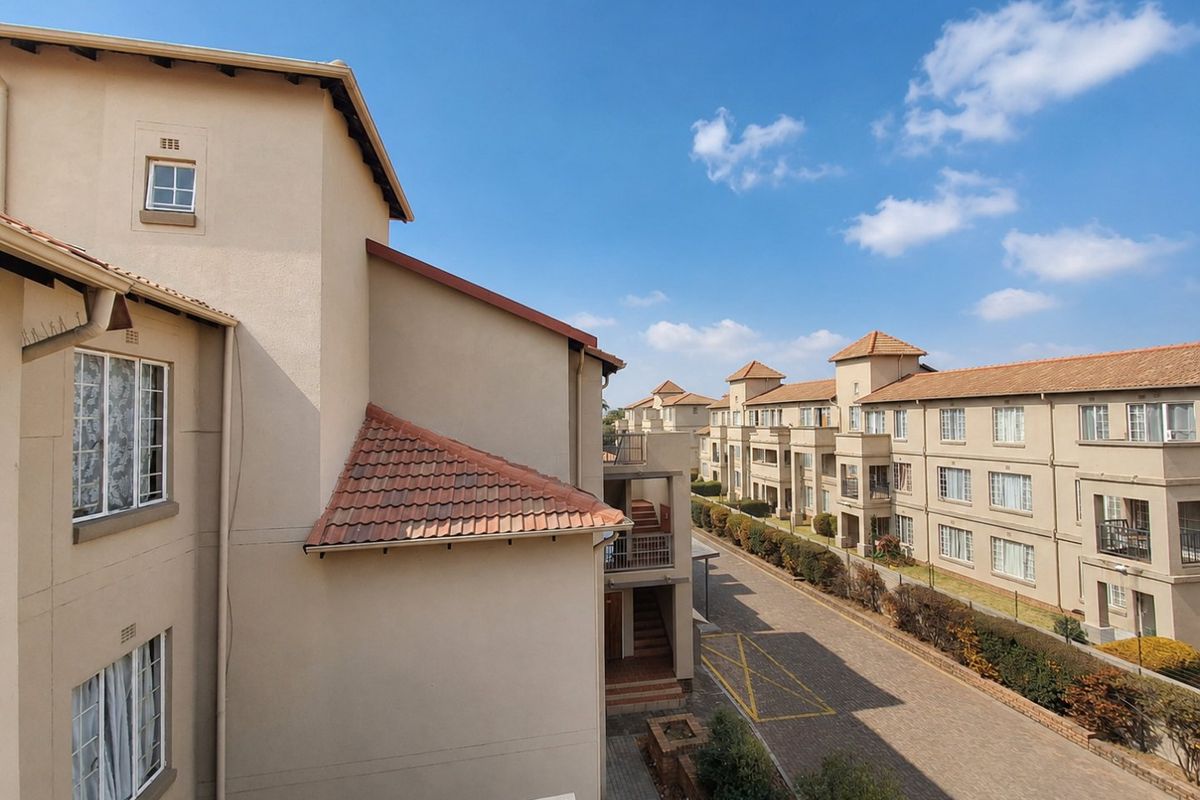 An elevated view of the apartment complex exterior, showcasing the building facade, terracotta roofing, and the paved driveway area.