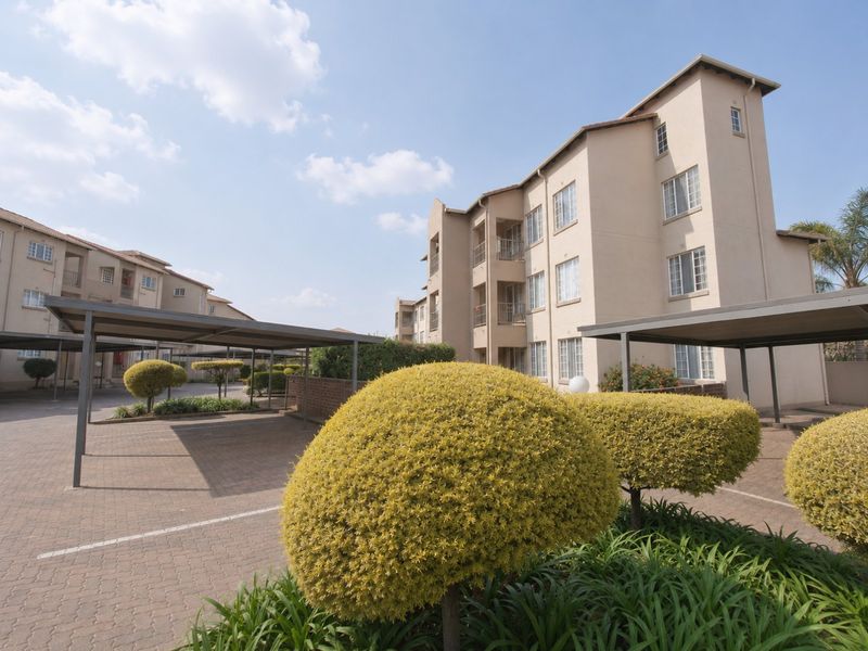 Exterior view of a multi-story apartment complex featuring paved parking areas with covered carports and well-maintained landscaped garden beds.