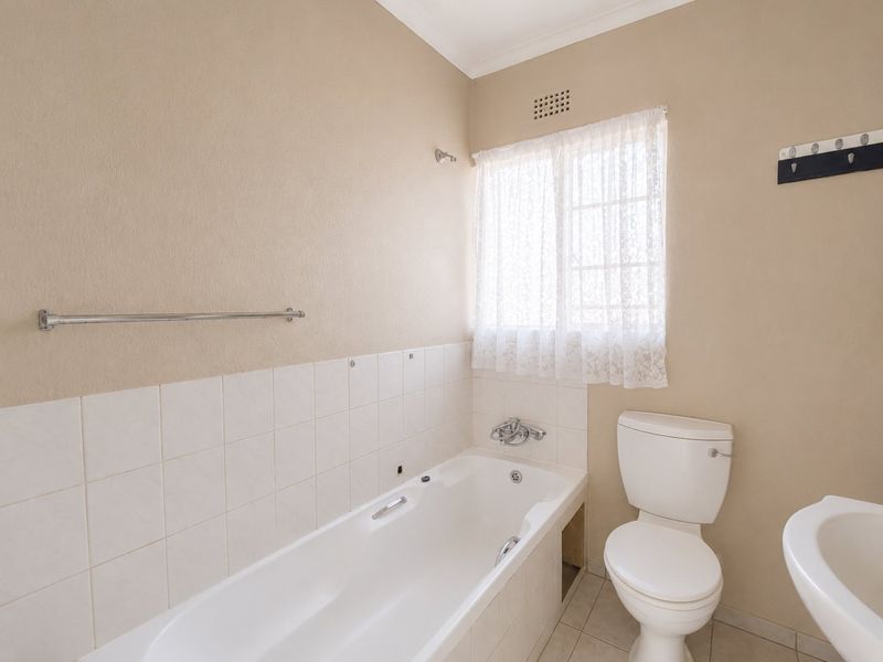 A functional bathroom featuring a standard bathtub, toilet, and washbasin with neutral wall finishes and tiled splashbacks.