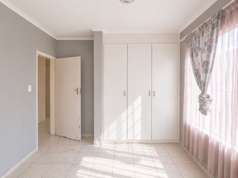 A bright, empty bedroom featuring built-in cupboards, tiled flooring, and neutral grey walls, offering a clean canvas for personalization.