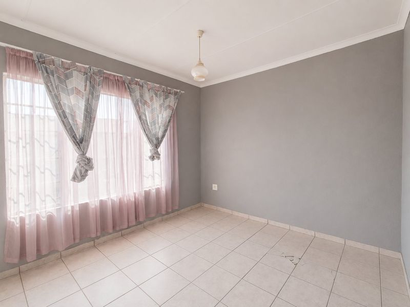 A bright, empty bedroom featuring neutral grey walls, tiled flooring, and a large window with curtains.