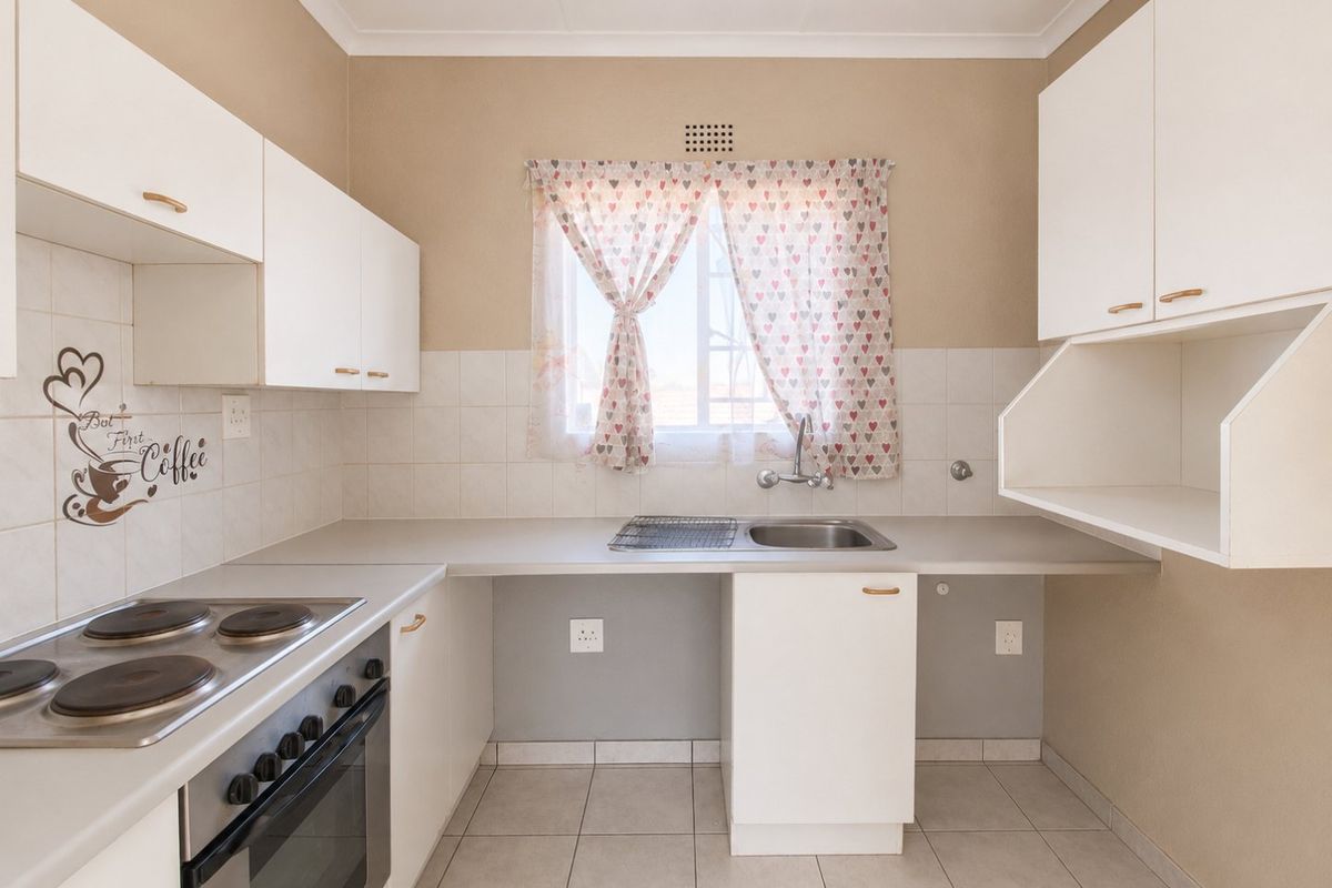 A functional kitchen featuring white built-in cabinetry, an electric hob with oven, tiled splashbacks, and tiled flooring.