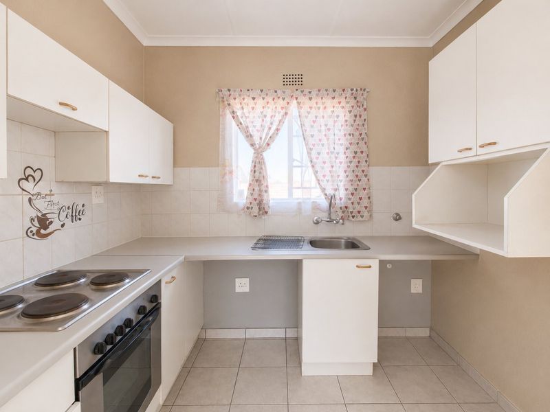 A functional kitchen featuring white built-in cabinetry, an electric hob with oven, tiled splashbacks, and tiled flooring.