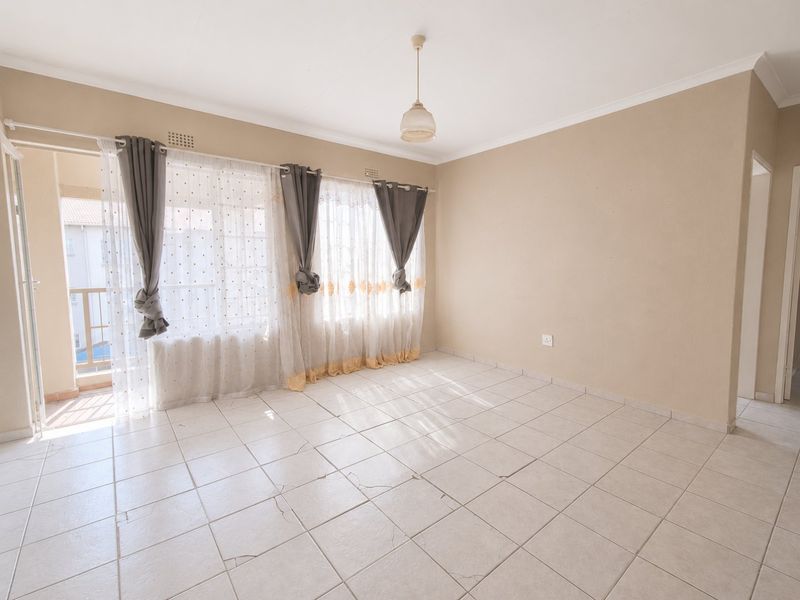 An empty living room featuring tiled flooring, neutral walls, and direct access to a private balcony through a sliding glass door.
