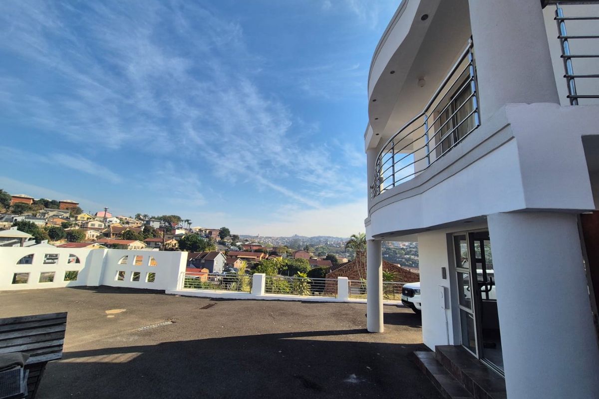 Rear exterior view featuring a curved balcony with stainless steel balustrades, overlooking a paved driveway and surrounding residential neighborhood.