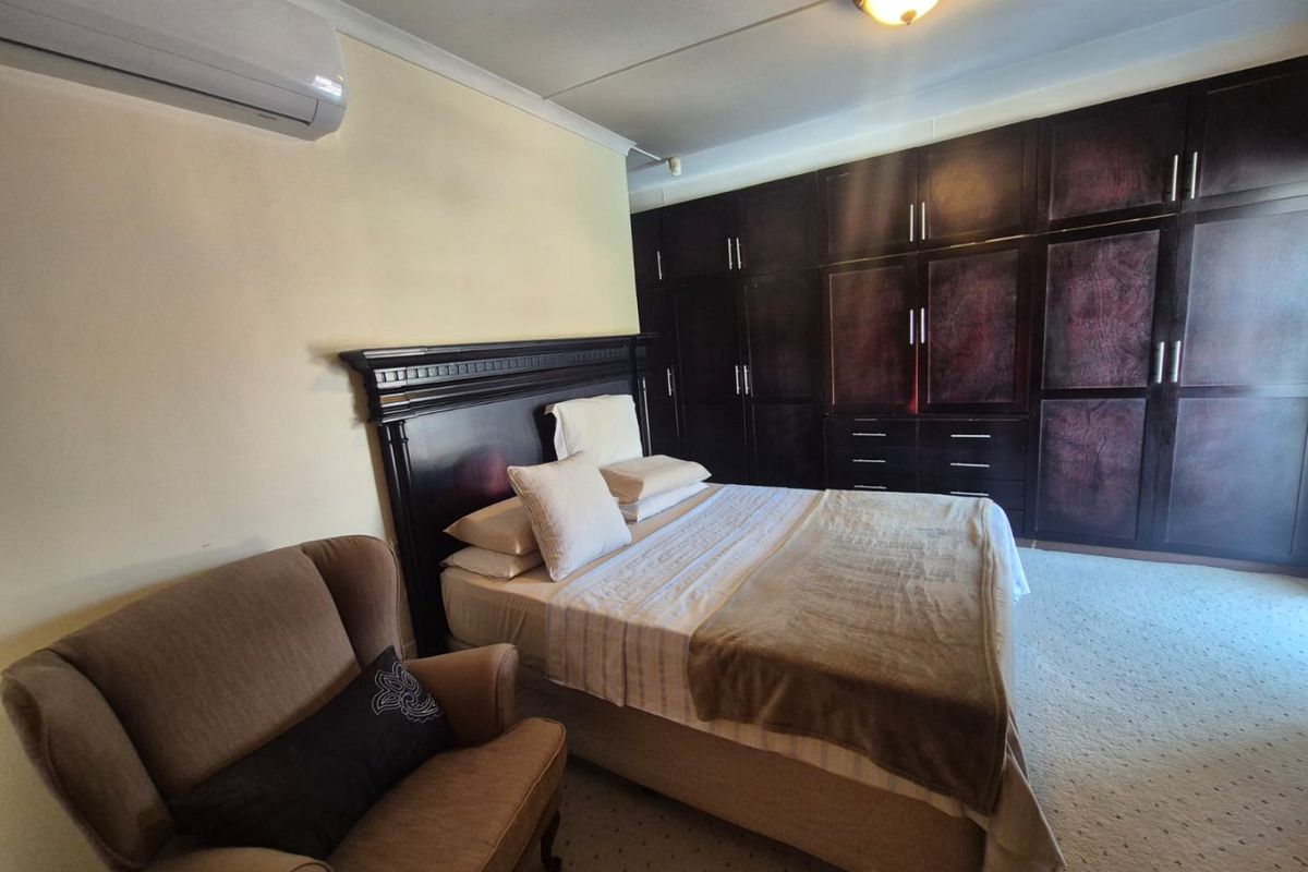 Spacious bedroom featuring extensive dark wood built-in cabinetry, carpeted flooring, and a wall-mounted air conditioning unit.