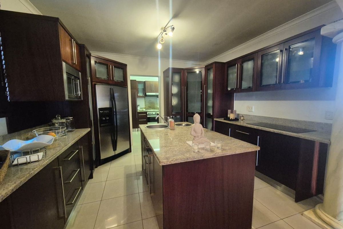Spacious kitchen featuring dark wood cabinetry, granite countertops, a central island with a double sink, and tiled flooring.