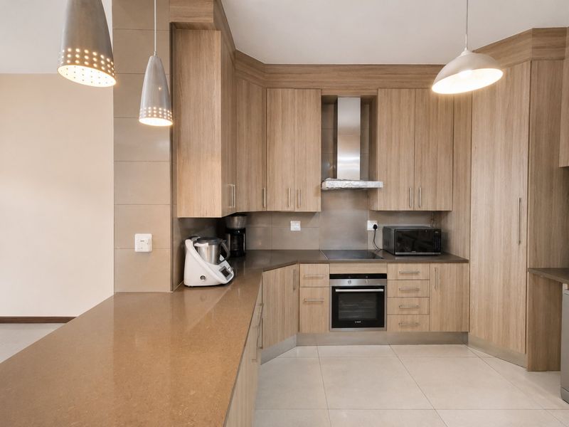 Modern kitchen featuring light wood cabinetry, stone countertops, integrated oven and hob, and stylish pendant lighting, offering a clean and functional workspace.