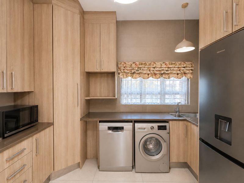 A modern, well-maintained kitchen featuring light wood-grain cabinetry, stone-look countertops, tiled backsplash, and integrated space for laundry appliances and a large refrigerator.