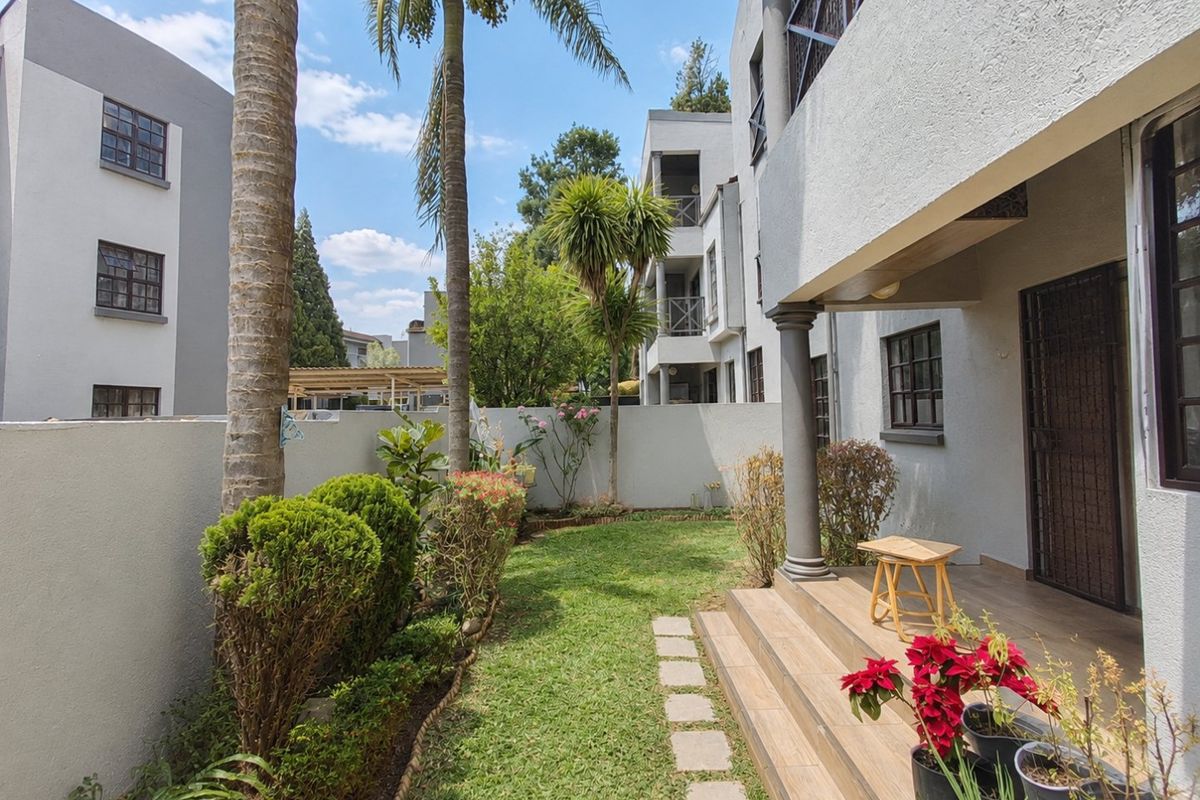 A private rear garden featuring a tiled patio area, concrete columns, and a well-maintained lawn enclosed by boundary walls.