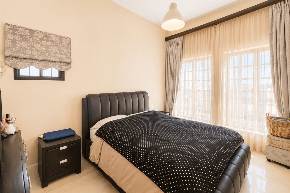 A well-lit bedroom featuring neutral tiled flooring, large windows with curtain tracks, and a central pendant light fixture.
