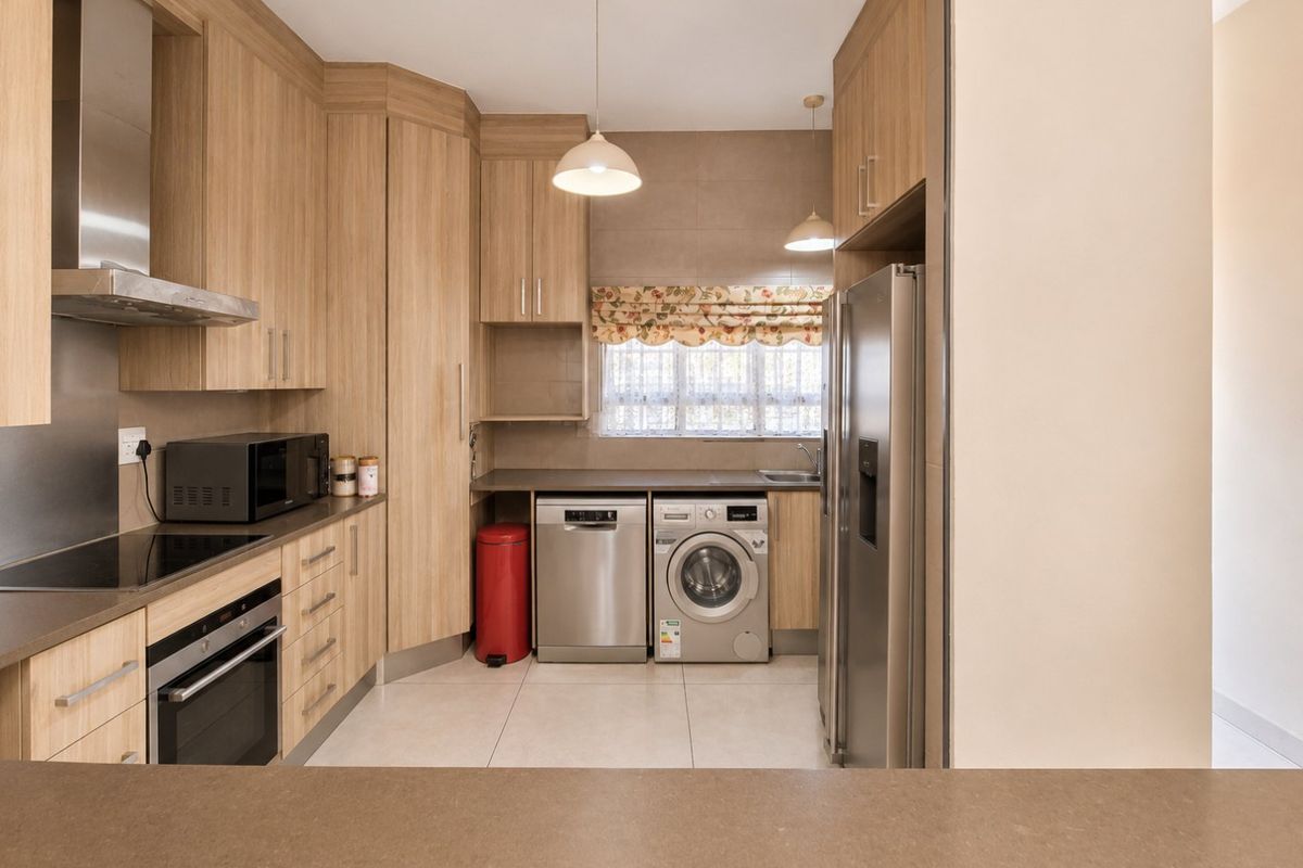 Modern kitchen featuring light wood cabinetry, integrated appliances, sleek countertops, and tiled flooring, offering a functional and well-maintained culinary space.