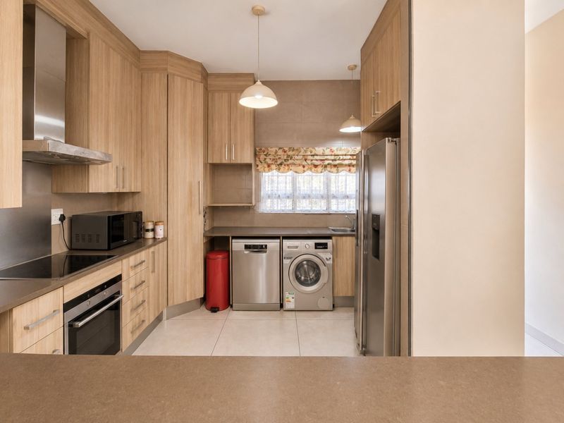 Modern kitchen featuring light wood cabinetry, integrated appliances, sleek countertops, and tiled flooring, offering a functional and well-maintained culinary space.