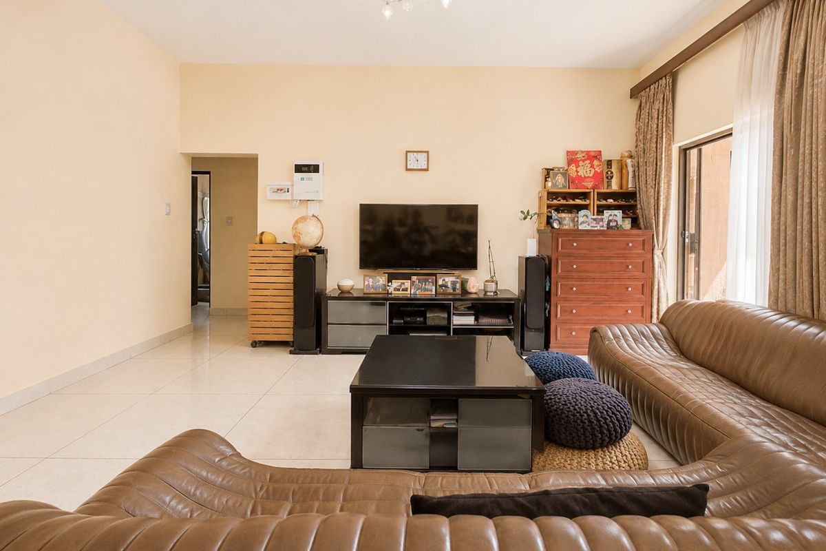 A spacious living room featuring neutral tiled flooring, ample natural light from a sliding glass door, and a clean, well-maintained interior finish.