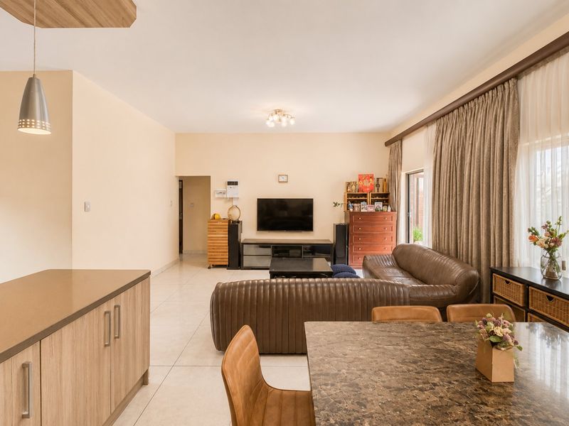 Spacious open-plan living and dining area featuring neutral walls, large format floor tiles, and ample natural light through floor-to-ceiling curtains.