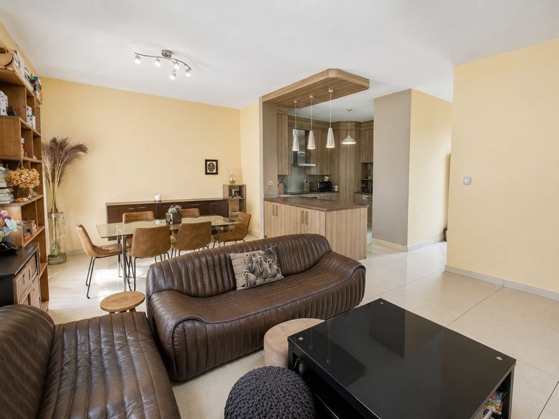 Spacious open-plan living and dining area featuring a modern kitchen with a central island, tiled flooring, and contemporary pendant lighting.