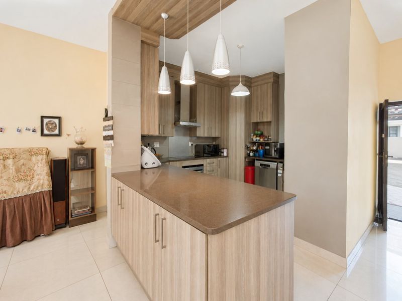 Open plan kitchen featuring a central island with stone countertops, modern laminate cabinetry, built-in appliances, and contemporary pendant lighting.